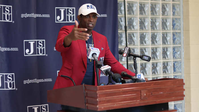Deion Sanders speaks at a podium after accepting the Jackson State football head coach position.